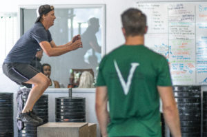 A male athlete doing a box jump while his coach watches.