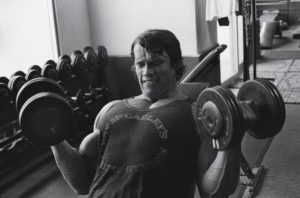 Young Arnold Schwarzenegger doing biceps curls.