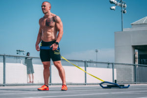 Shirtless male athlete getting ready to drag a sled at the track.