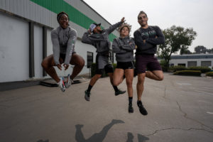 Members of the Invictus weightlifting team jump in unison while posing outside the gym.