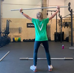 A female athlete facing away from the camera doing a PVC warm-up for snatching.