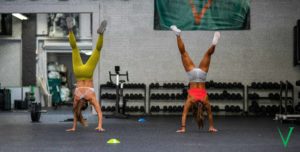 Two female athletes walking on their hands around cones.