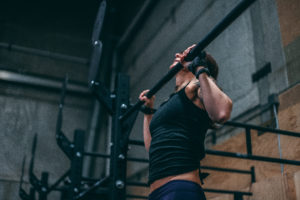 Female athlete with her chin over the bar at the top of a strict pull-up.