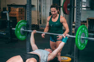 A female athlete spots another female on the bench press.