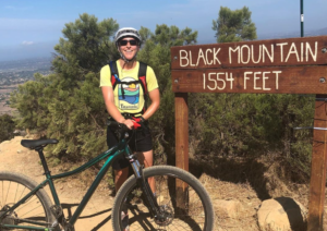 Coach Kir and her mountain bike standing at the top of Black Mountain by the elevation sign.