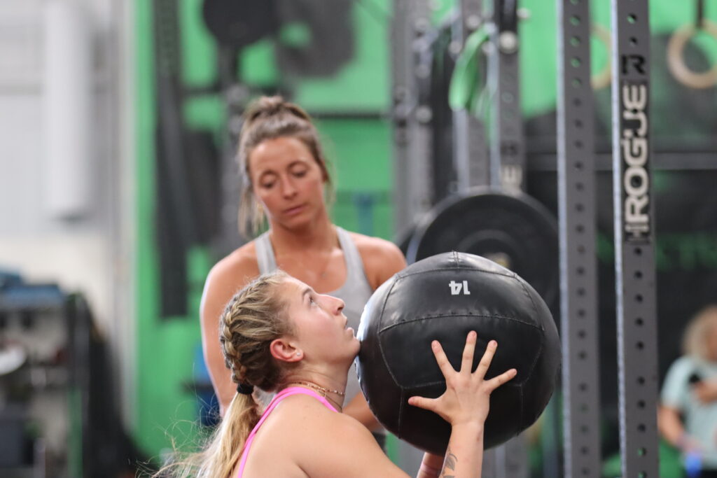 A coach watching over her athlete as she does wall balls. 